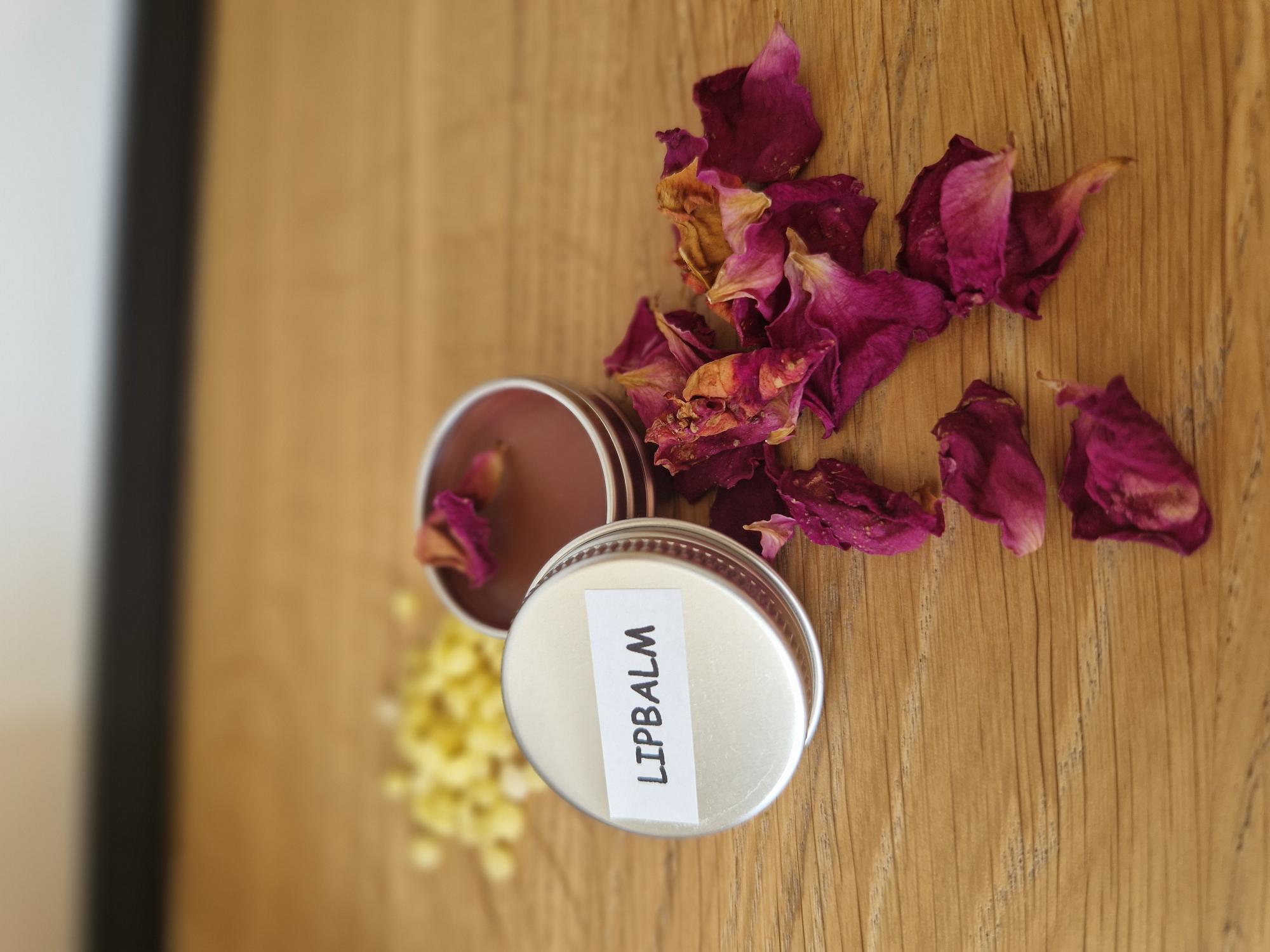 Zelfgemaakte lipzalf in een metalen potje met handgeschreven labeltje, tussen rozenblaadjes en gele bloemen